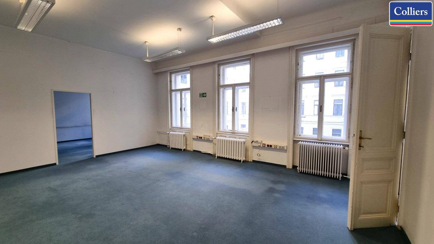 Großes, leeres Büro mit blauem Teppichboden, mehreren Fenstern und offener Tür.