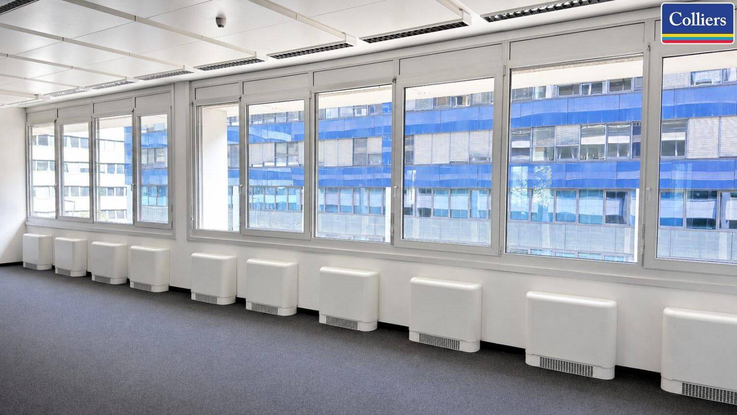 Langes, helles Büro mit einer durchgehenden Fensterfront und Heizkörpern unter den Fenstern.