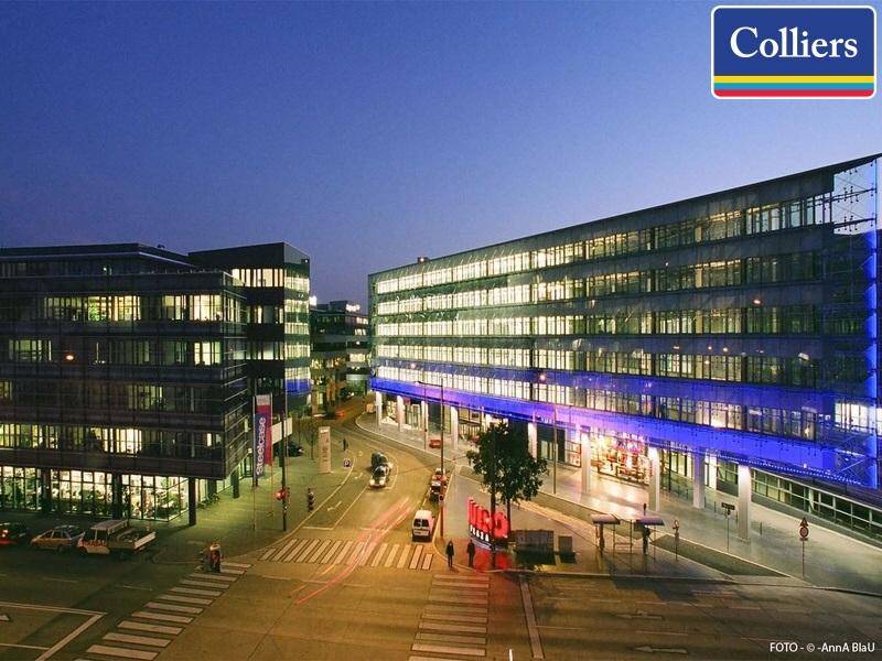 Moderne Bürogebäude mit beleuchteten Fassaden bei Nacht, umgeben von einer städtischen Straße.