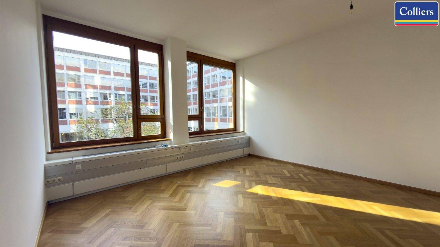 Leerer Büroraum mit großen Fenstern und klassischem Fischgrätparkett, bereit zur individuellen Gestaltung.