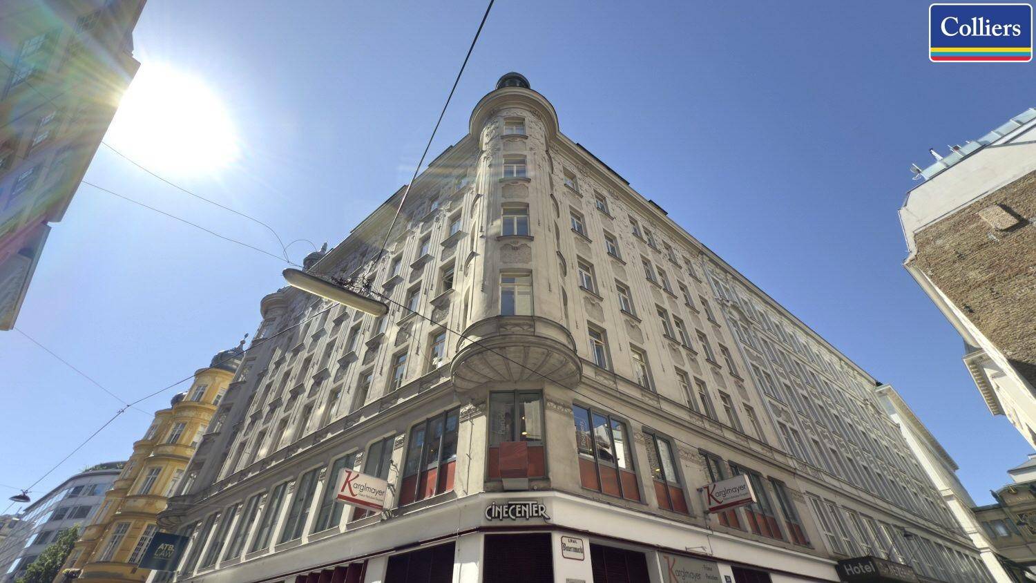 Historisches Eckgebäude mit vielen Fenstern und Geschäften im Erdgeschoss unter strahlender Sonne.
