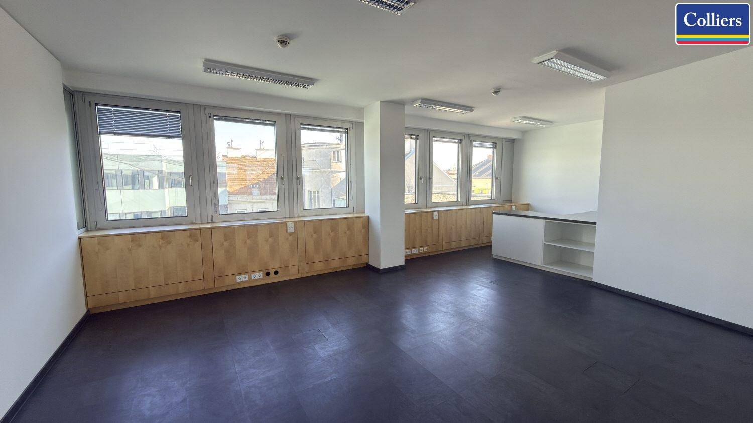 Geräumiges Büro mit dunklem Bodenbelag, weißen Wänden und breiter Fensterfront.