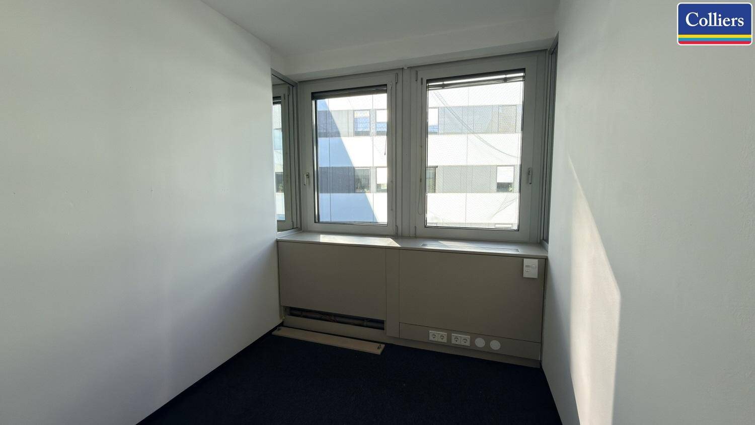 Kompaktes Büro mit Teppichboden und Fenstern, die einen Blick auf die Umgebung ermöglichen.