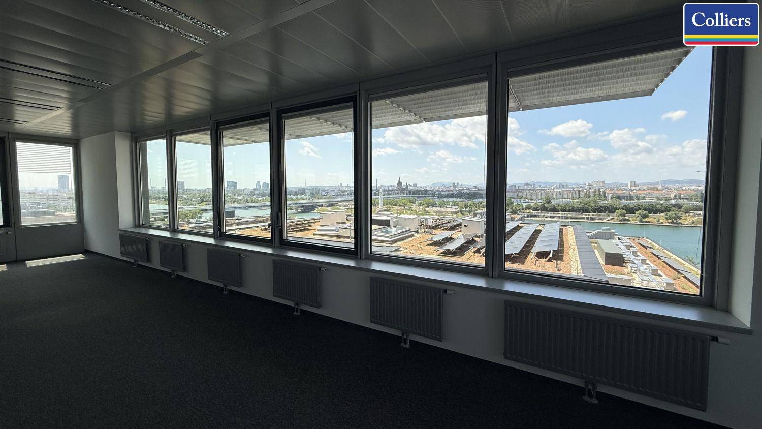 Büro mit weitem Ausblick auf die Stadt und den Fluss, ausgestattet mit Heizkörpern unter den Fenstern.