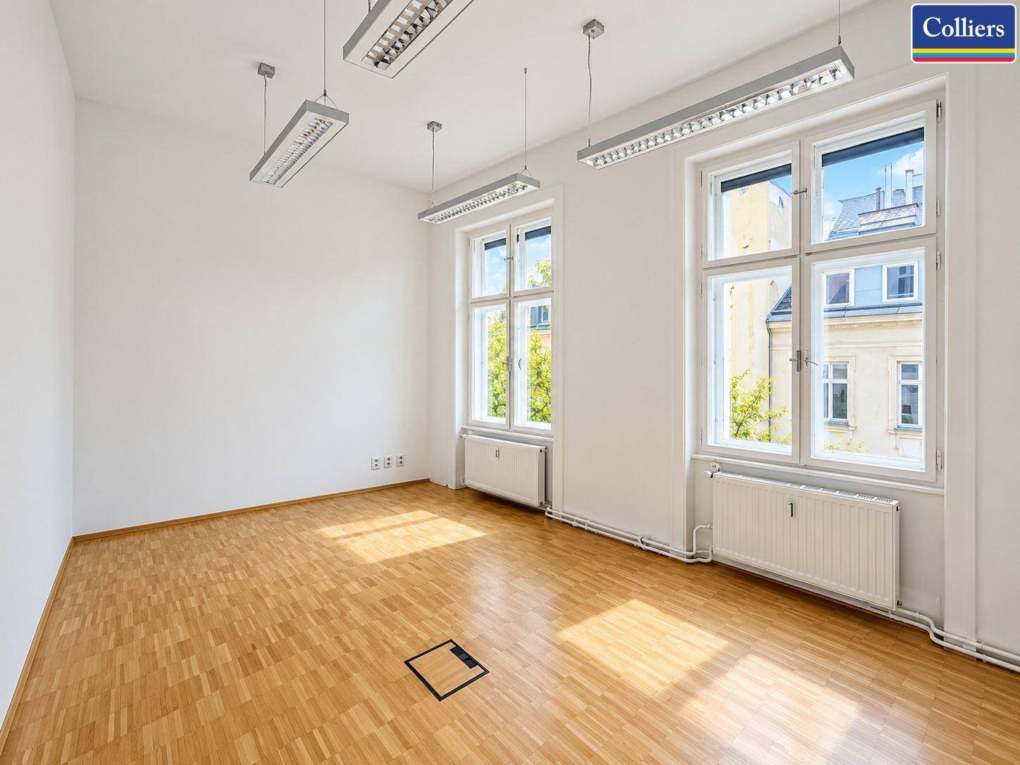 Leeres Büro mit Parkettboden und hohen Fenstern, bereit für individuelle Einrichtung.