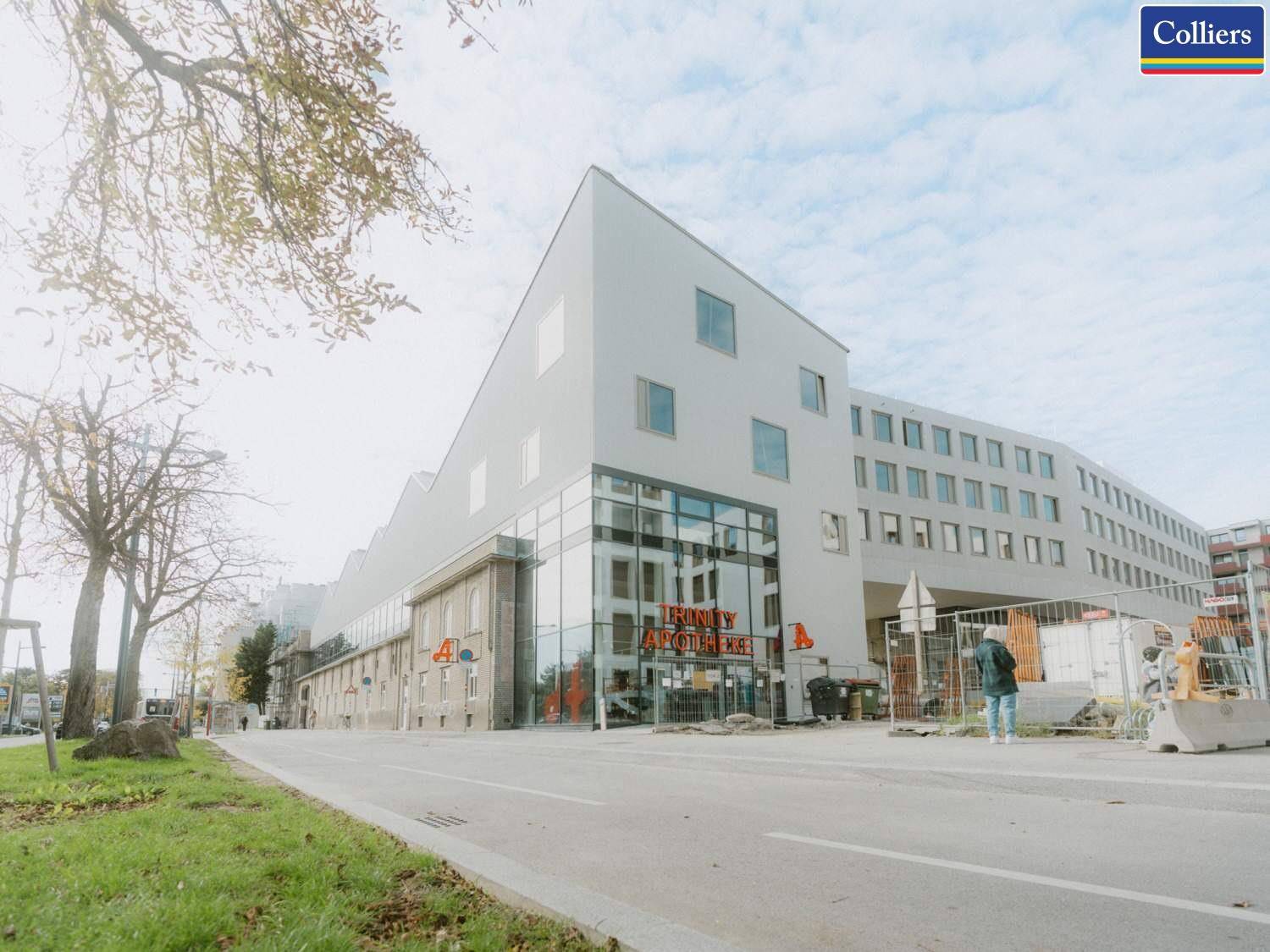 Moderne Geschäftsgebäudeansicht von der Straße mit großen Glasflächen im Erdgeschoss und umliegender Bebauung.
