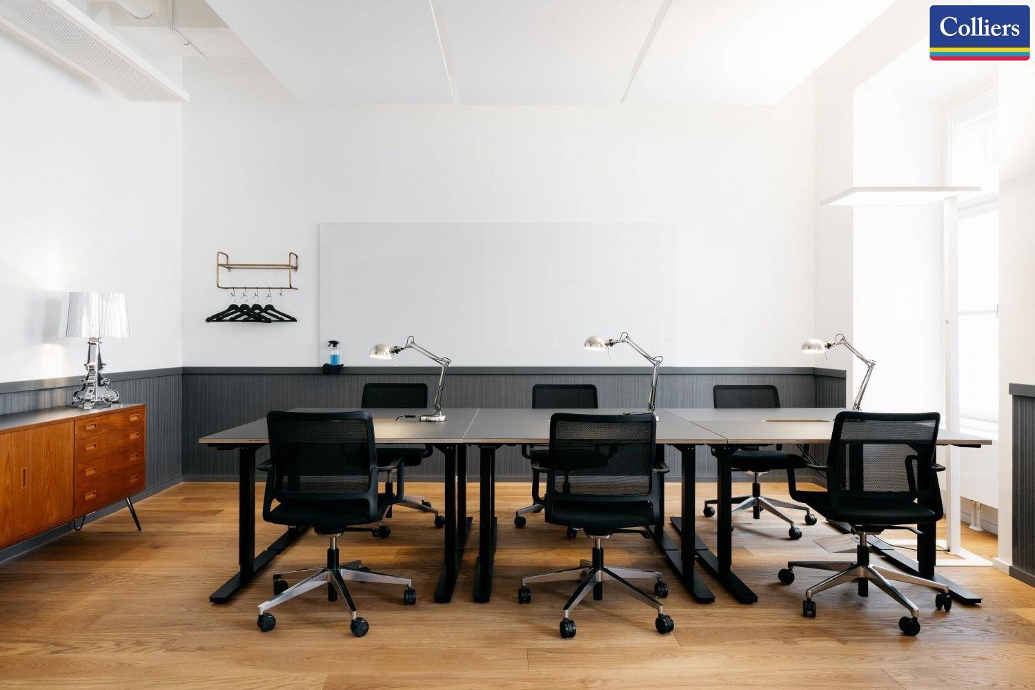 Heller Büroraum mit mehreren Schreibtischen, ergonomischen Stühlen und einer großen Whiteboard-Wand.