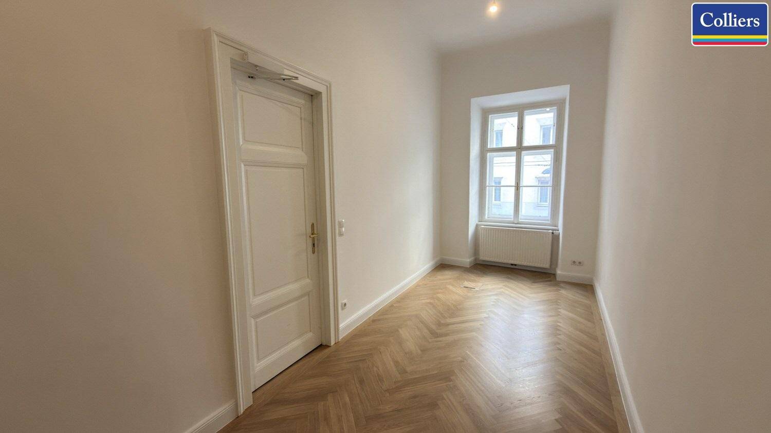 Schmaler, heller Raum mit Fischgrätparkett und einem Fenster, geeignet als Einzelbüro oder Archiv.