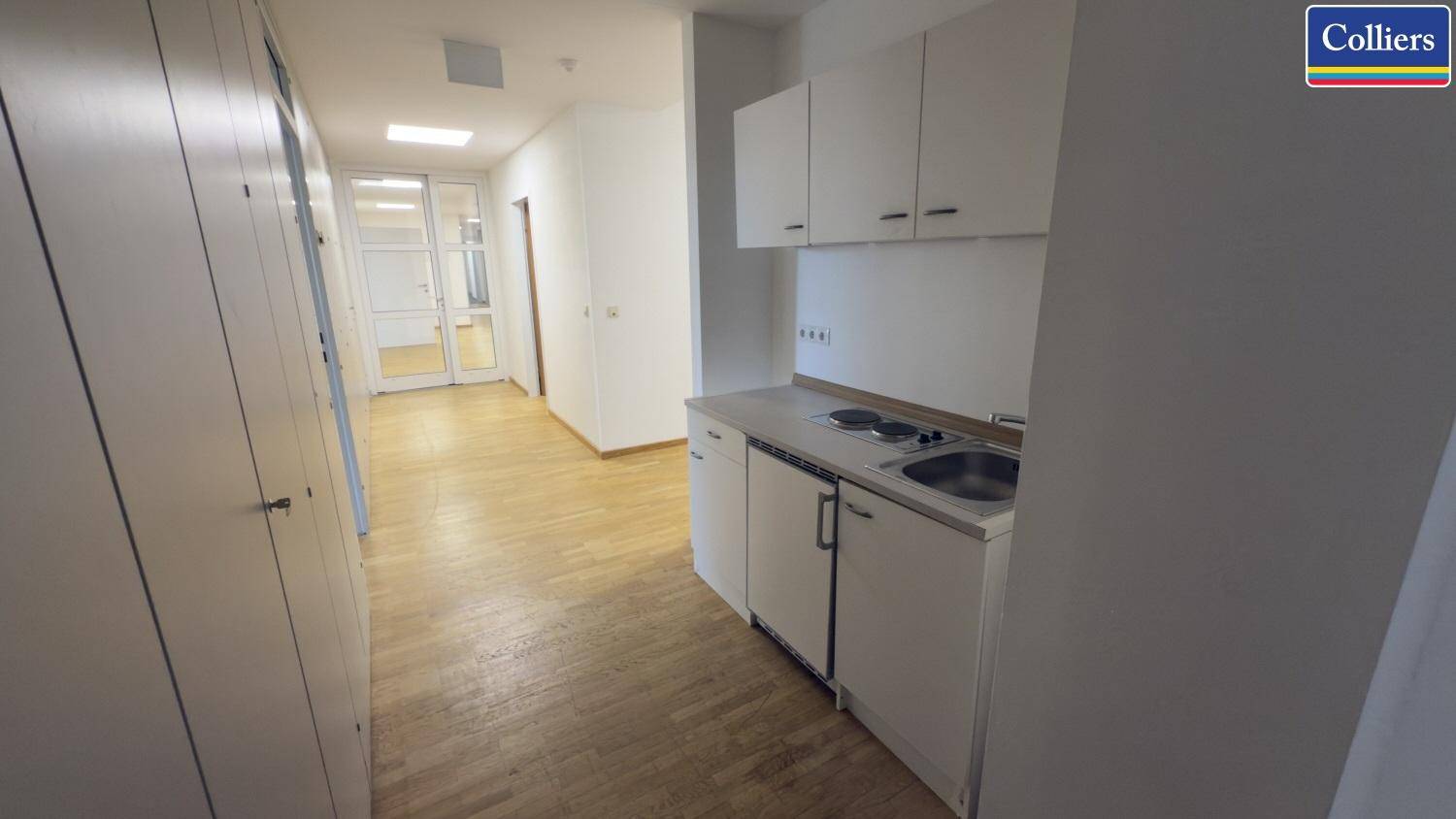 Heller Flur mit integrierter Teeküche, ausgestattet mit weißen Schränken, Spüle und Kochplatten.