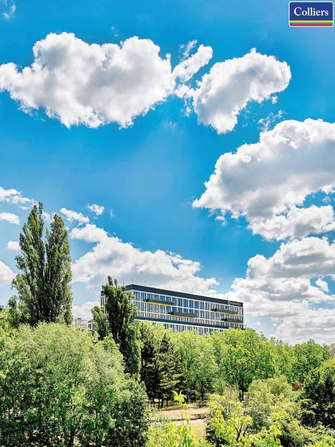 Modernes Bürogebäude umgeben von üppigem Grün und Bäumen unter einem blauen Himmel.