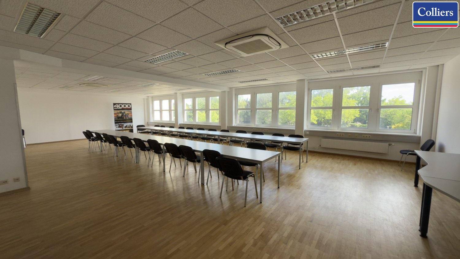 Großer Konferenzraum mit Holzfußboden, vielen Fenstern und Bestuhlung für Veranstaltungen oder Schulungen.