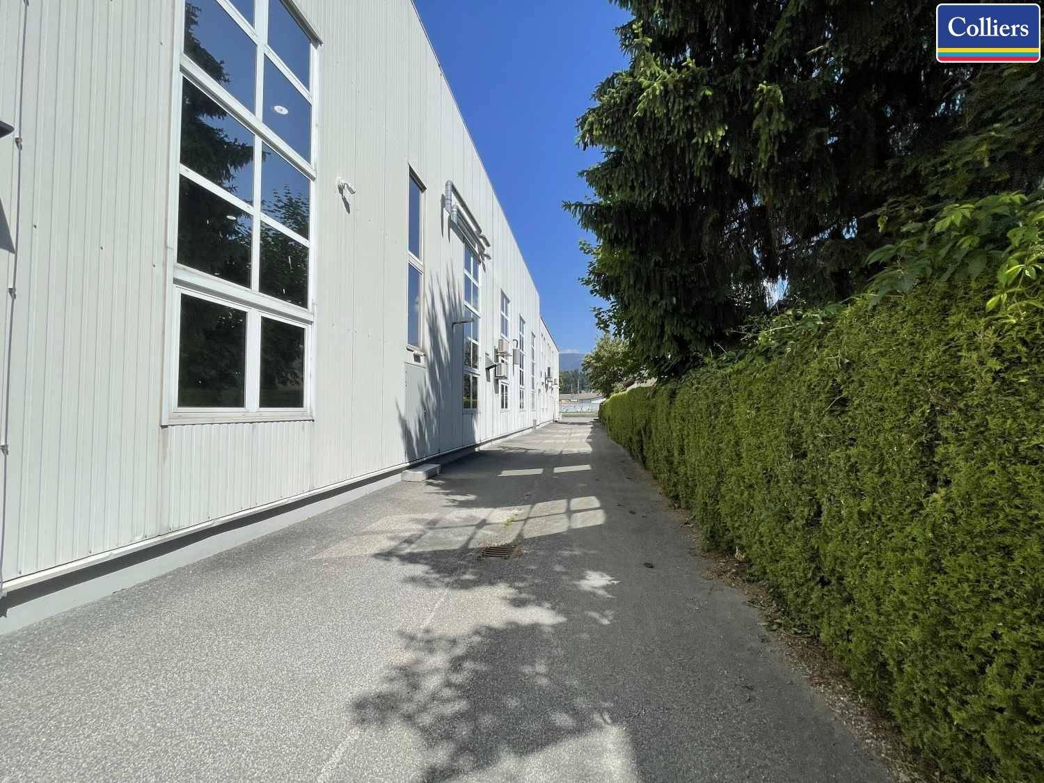 Gehweg entlang der Gebäudeseite, gesäumt von einer gepflegten Hecke und Bäumen.