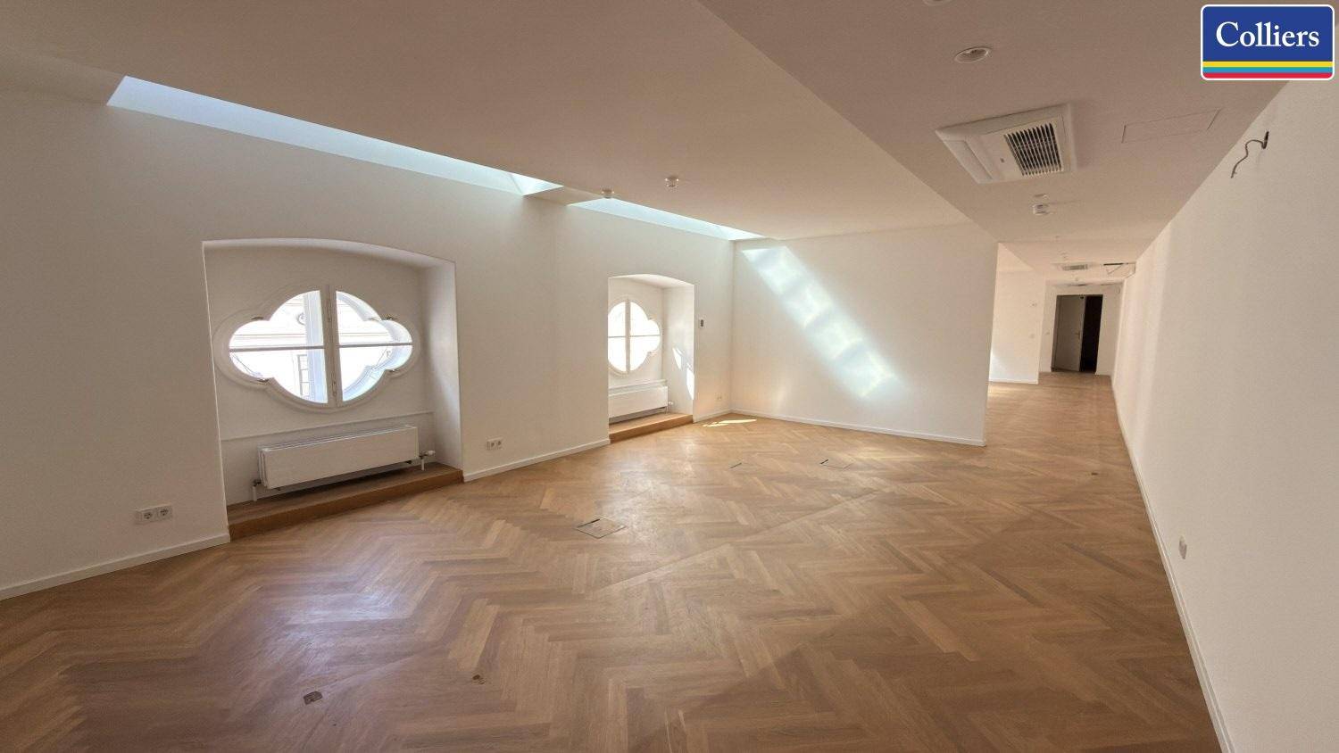 Geräumiger Büroraum mit Fischgrätparkett, einzigartigen Fenstern und Klimaanlage, die den Raum mit Sonnenlicht füllen.