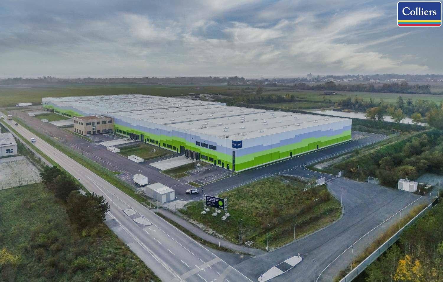 Weitläufige Luftaufnahme eines großen Logistikkomplexes mit umliegenden Feldern und Zufahrtsstraßen.