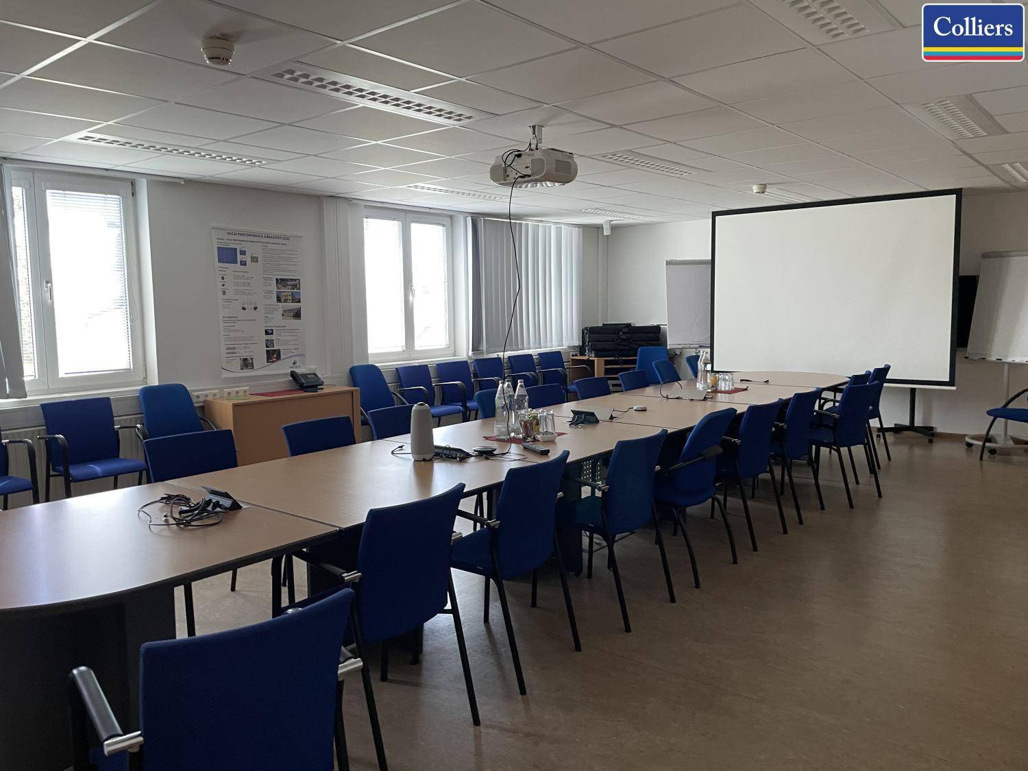 Großer Konferenzraum mit einem langen Tisch, vielen Stühlen und einem Beamer für Präsentationen.