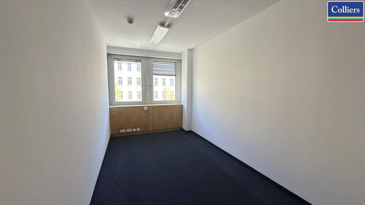 Kompaktes Büro mit Teppichboden und Blick auf die umliegenden Gebäude, ausgestattet mit Jalousien.