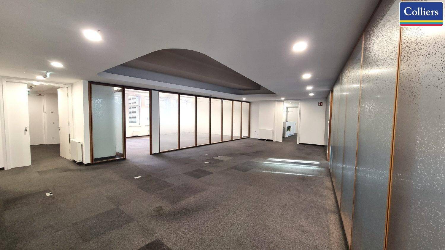 Großes, offenes Büro mit Teppichboden und Glaswänden, das Flexibilität und Helligkeit bietet.