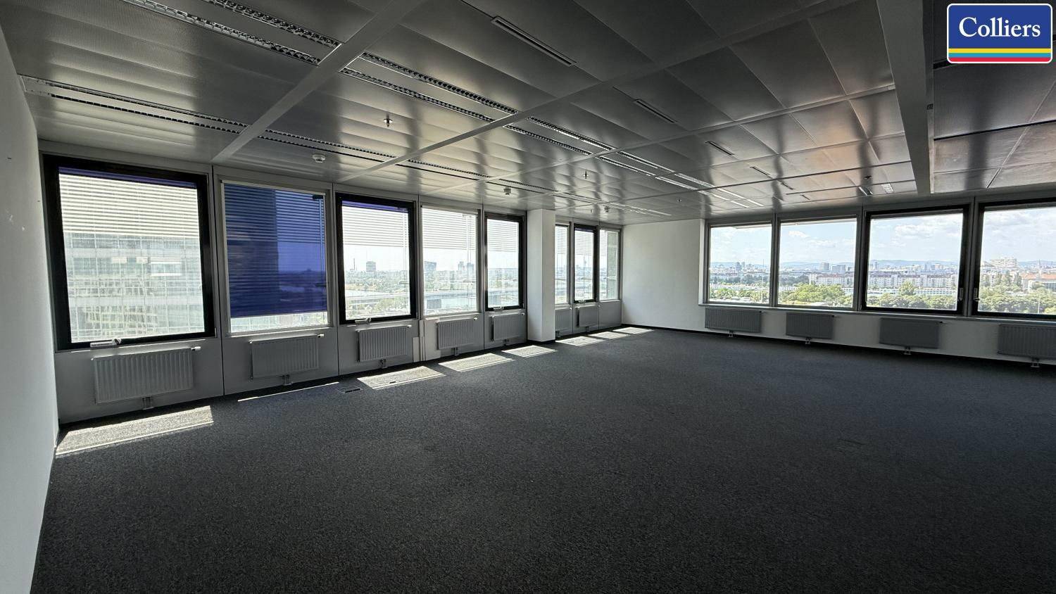 Weitläufiges Büro mit Teppichboden, vielen Fenstern und Panoramablick über die Stadt.
