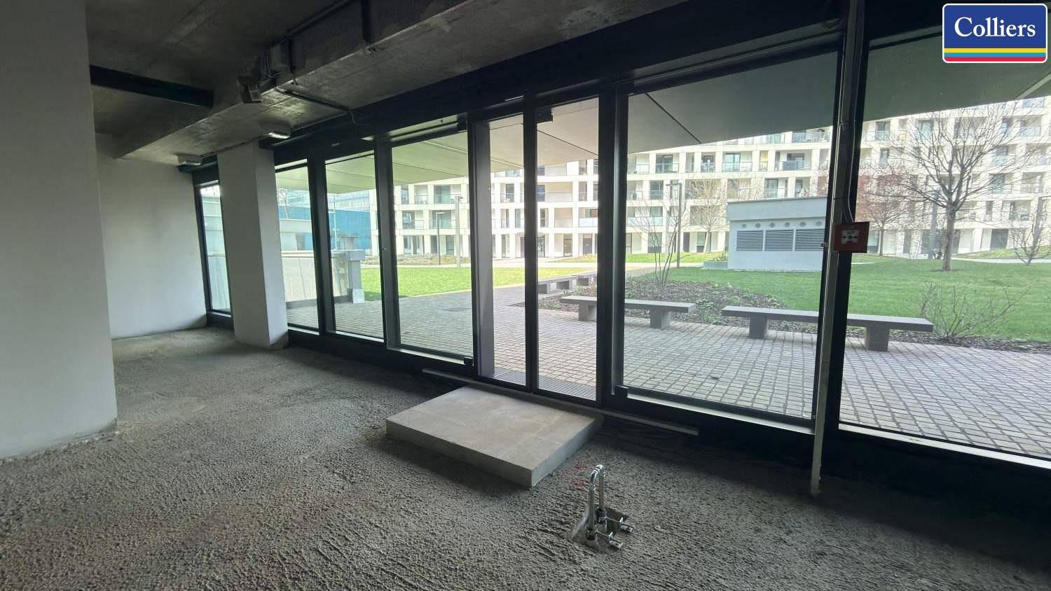 Innenansicht eines Gewerberaums mit bodentiefen Fenstern, die den Blick auf den gepflasterten Außenbereich freigeben.