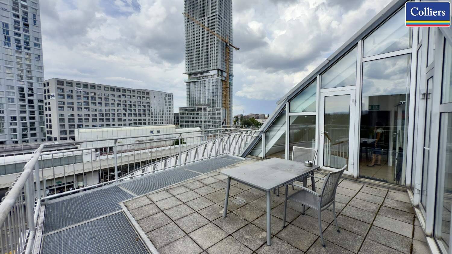 Geräumige Dachterrasse mit Sitzgelegenheiten und Zugang zu einem Gebäude mit großer Glasfassade.