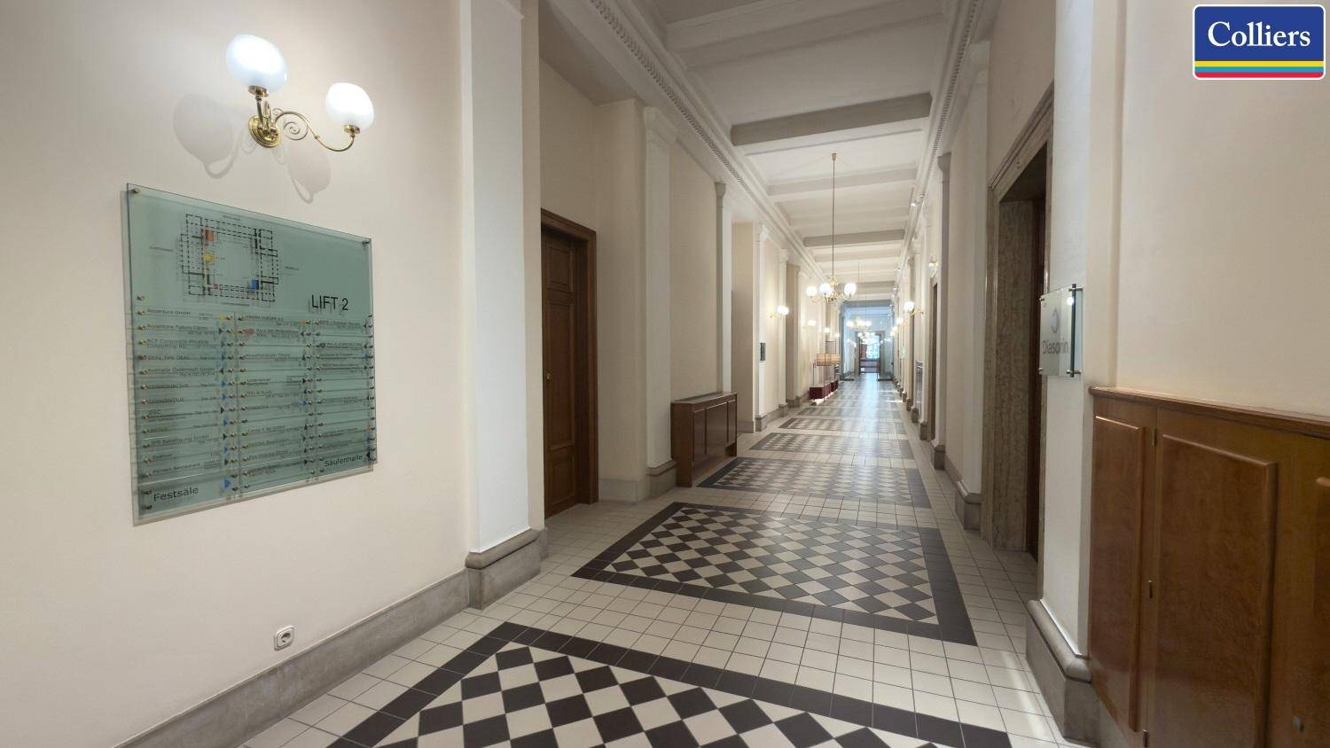 Langer Flur mit Schachbrettmuster-Fliesenboden und klassischer Wandgestaltung, führt zu den Büros.