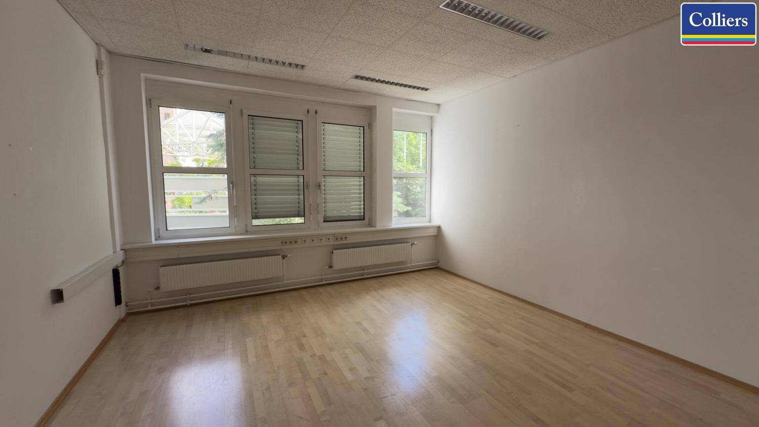 Helles, leeres Büro mit großen Fenstern und Jalousien, die den Raum mit natürlichem Licht versorgen.