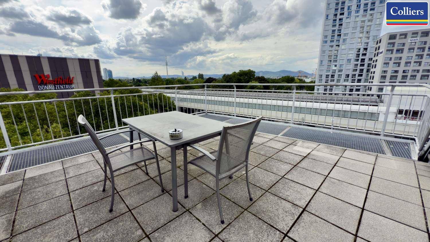 Möblierte Dachterrasse mit Steinfliesen, einem Tisch und Stühlen, bietet einen weiten Blick über die Stadt.