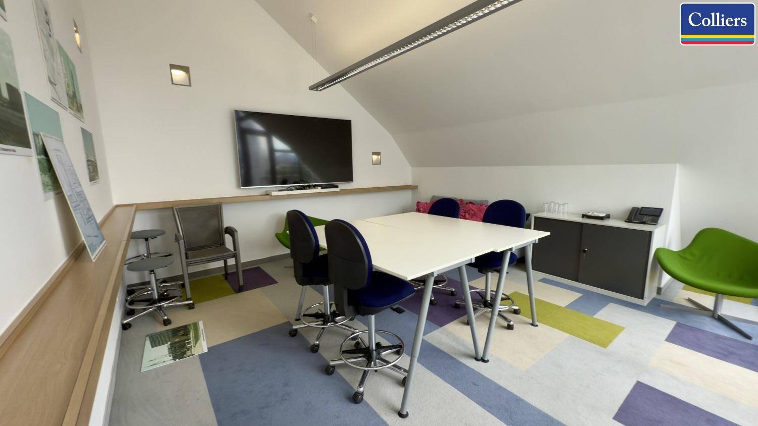 Moderner Besprechungsraum im Dachgeschoss mit schrägen Wänden und farbenfrohem Teppichboden.