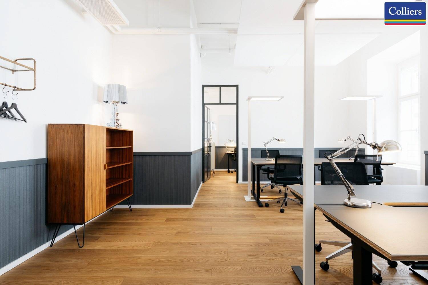 Heller offener Bürobereich mit Holzboden, modernen Möbeln und Blick auf weitere Arbeitsplätze.