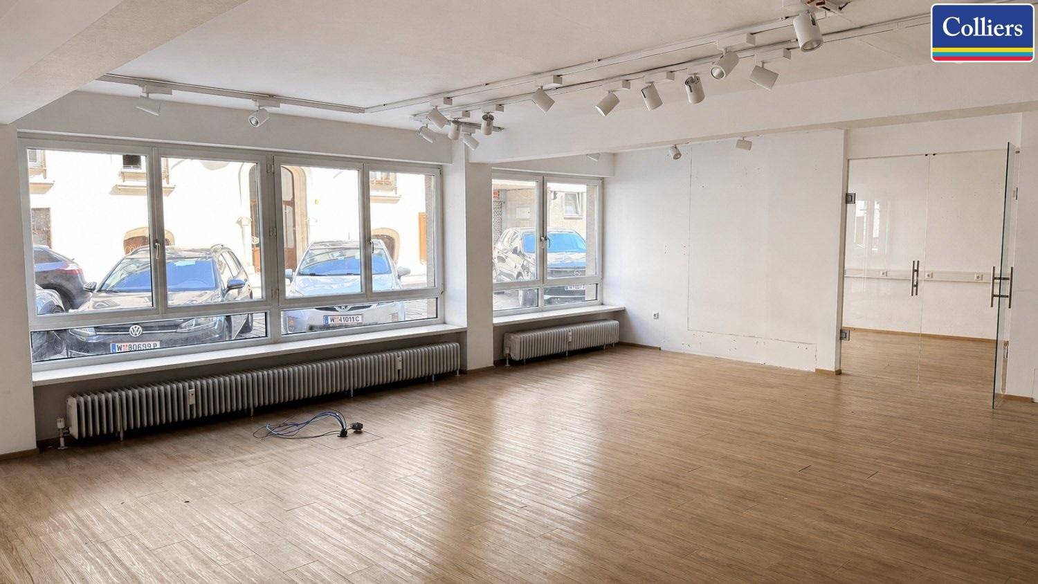Heller Geschäftsraum mit großen Fenstern zur Straße und moderner Beleuchtung an der Decke, bereit zur Nutzung.