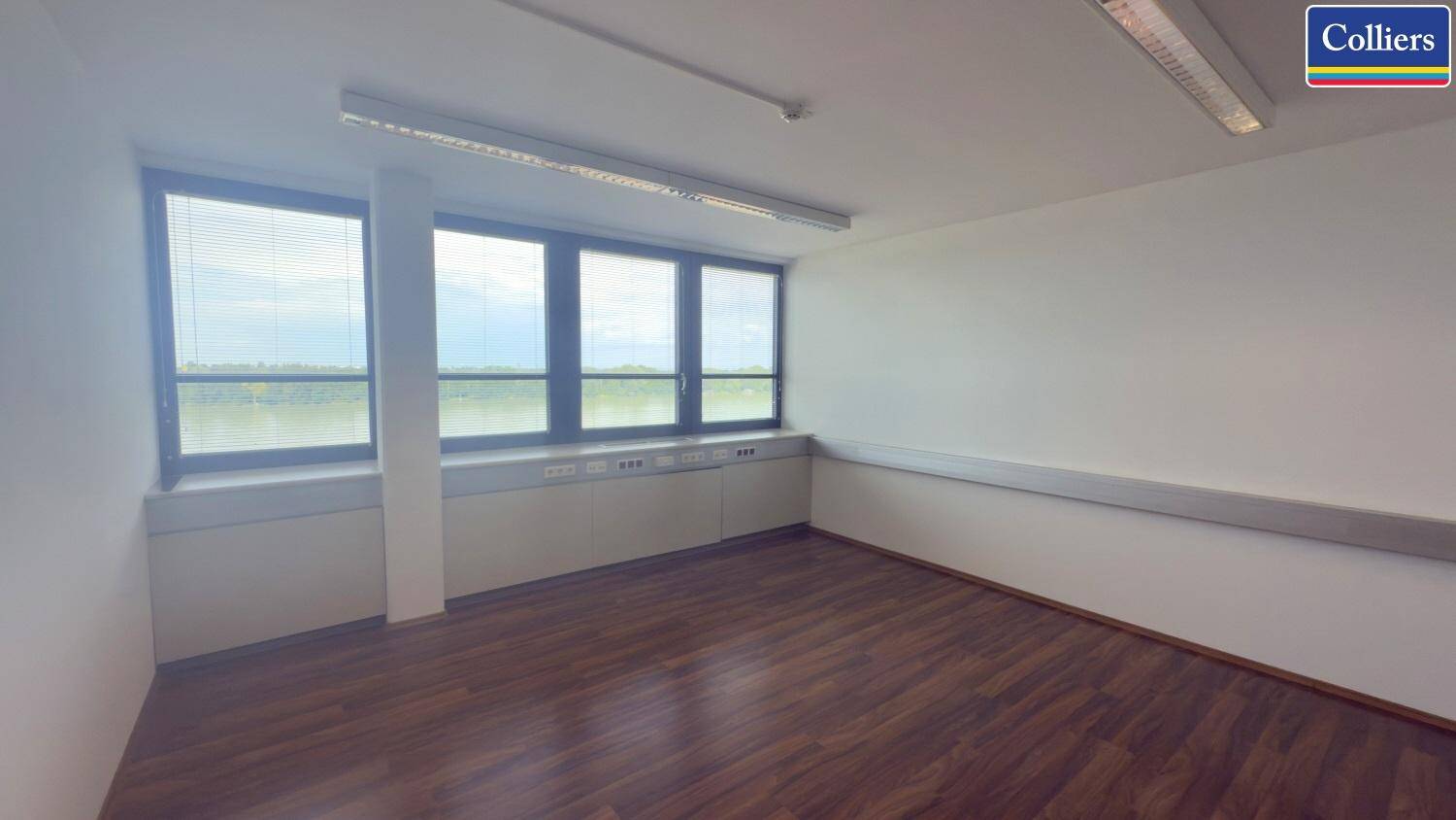 Büro mit Holzboden und einer breiten Fensterfront, die viel Tageslicht und einen weiten Blick ermöglicht.
