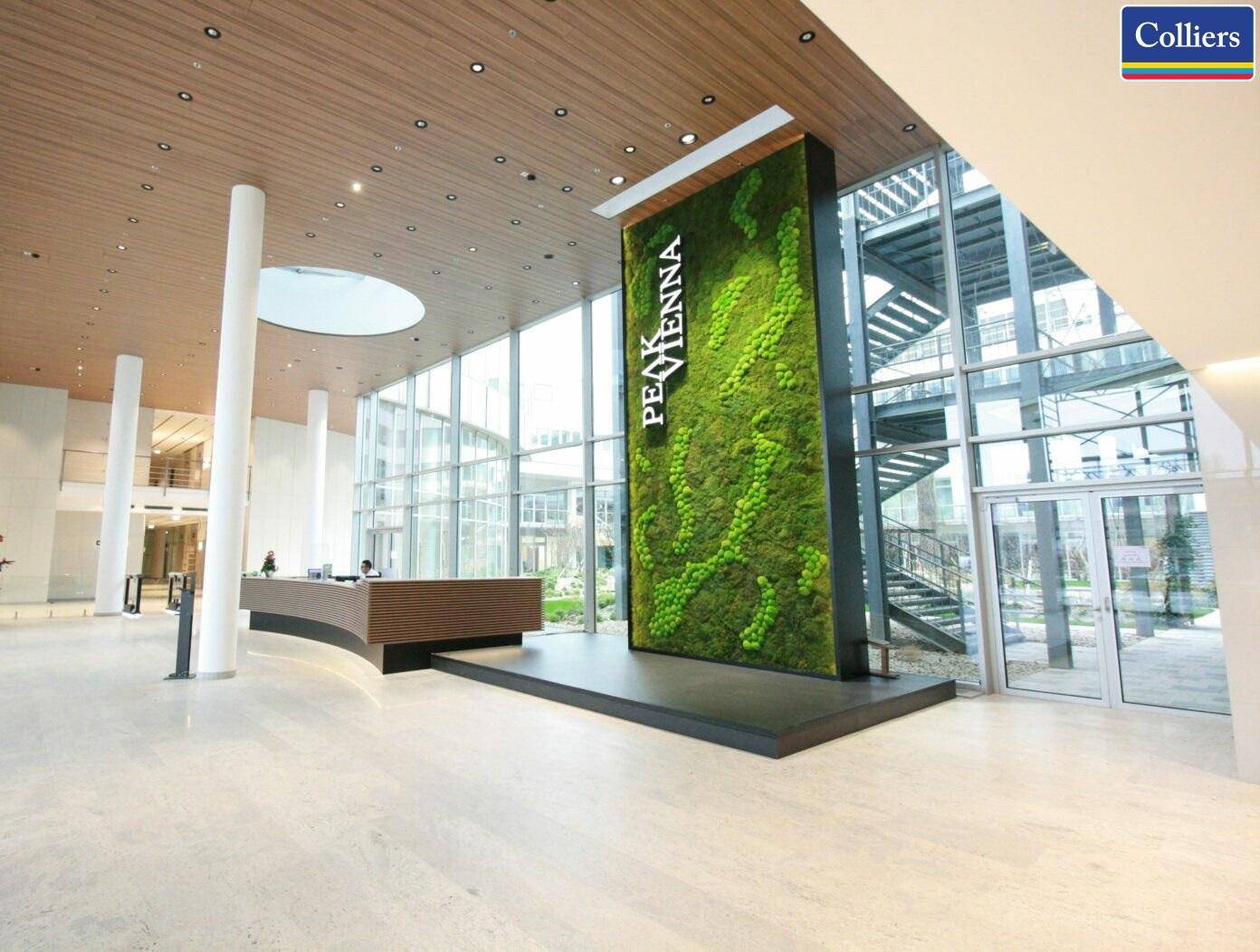 Eindrucksvolle Lobby mit hoher Decke, moderner Rezeption und einer auffälligen grünen Mooswand als Designelement.