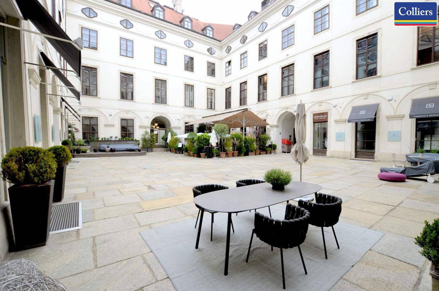 Malerischer Innenhof mit Sitzgelegenheiten und Pflanzen, umgeben von historischen Gebäuden und gepflastertem Boden.