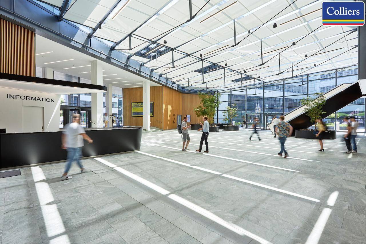 Weitläufige, helle Lobby mit Informationsschalter, moderner Architektur und viel Tageslicht durch die Glasfronten.