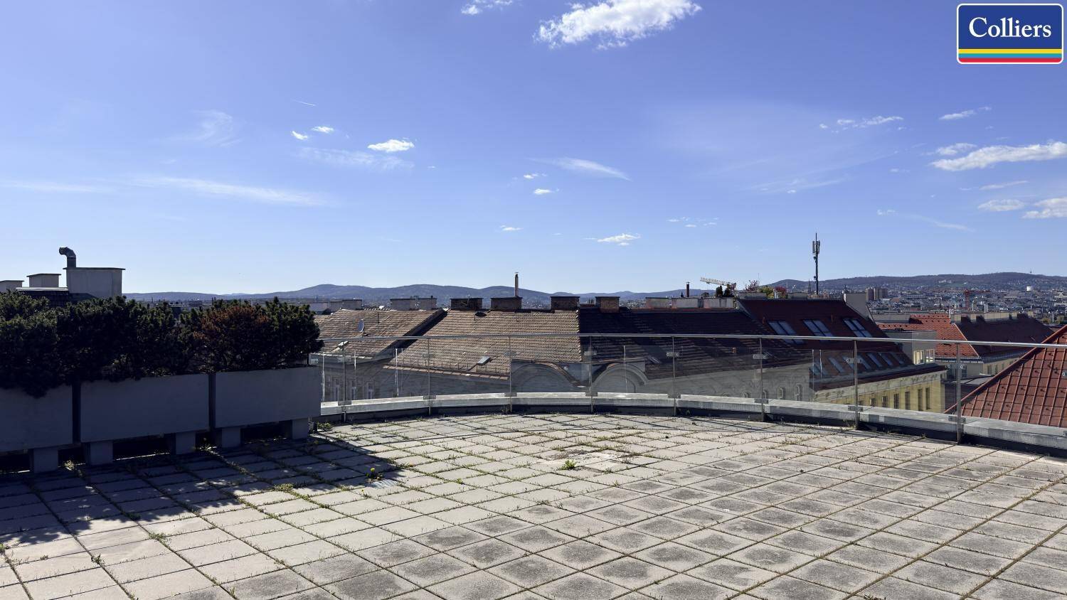 Weitläufige Dachterrasse mit Steinplatten und Panoramablick über die Stadt unter strahlend blauem Himmel.