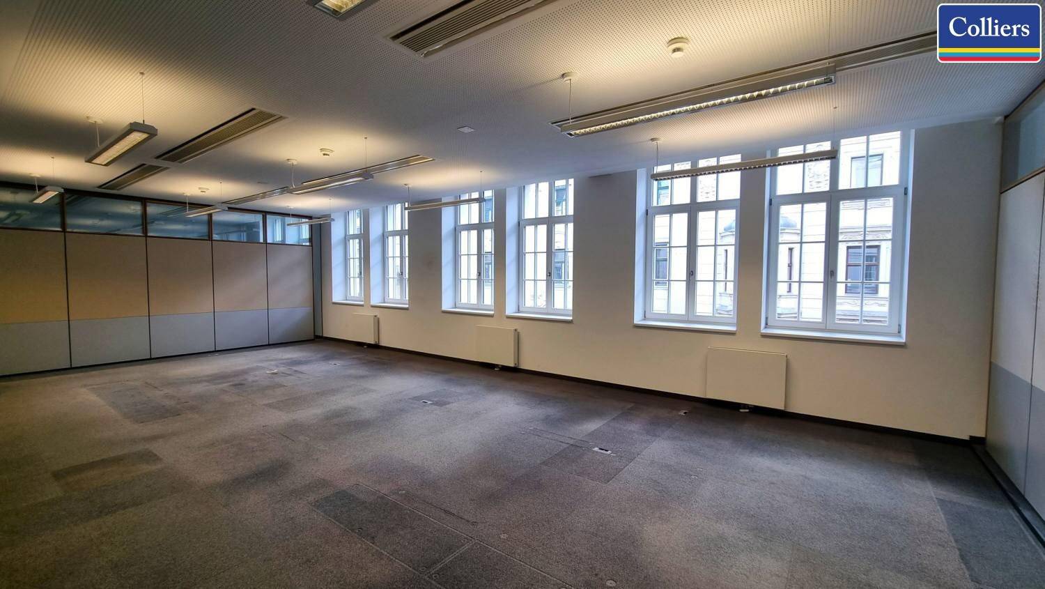 Großes Büro mit mehreren Fenstern, Teppichboden und Deckenbeleuchtung, geeignet für Großraumbüros.