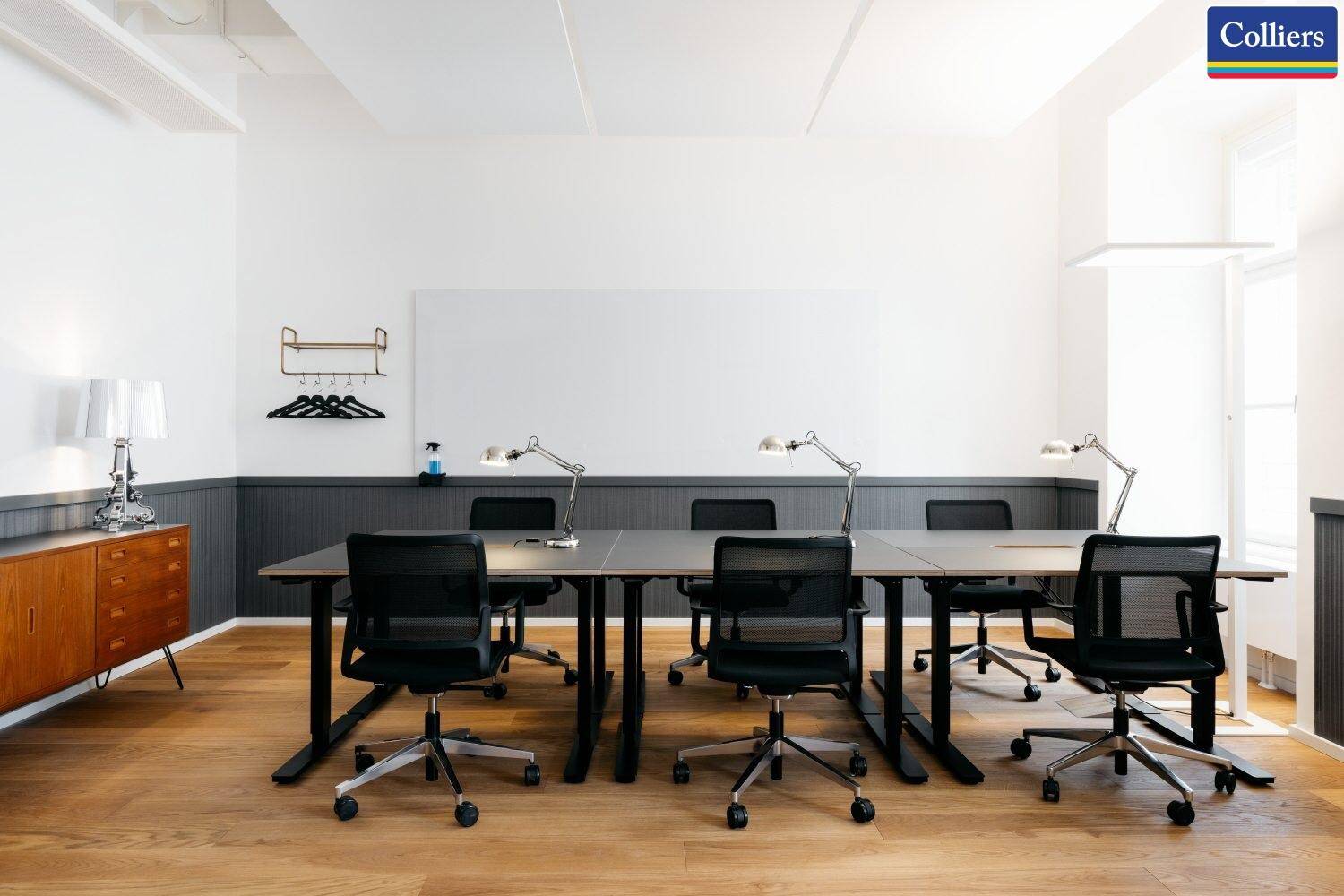 Geräumiger Büroraum mit mehreren Arbeitsplätzen, Whiteboard und einem Sideboard aus Holz.