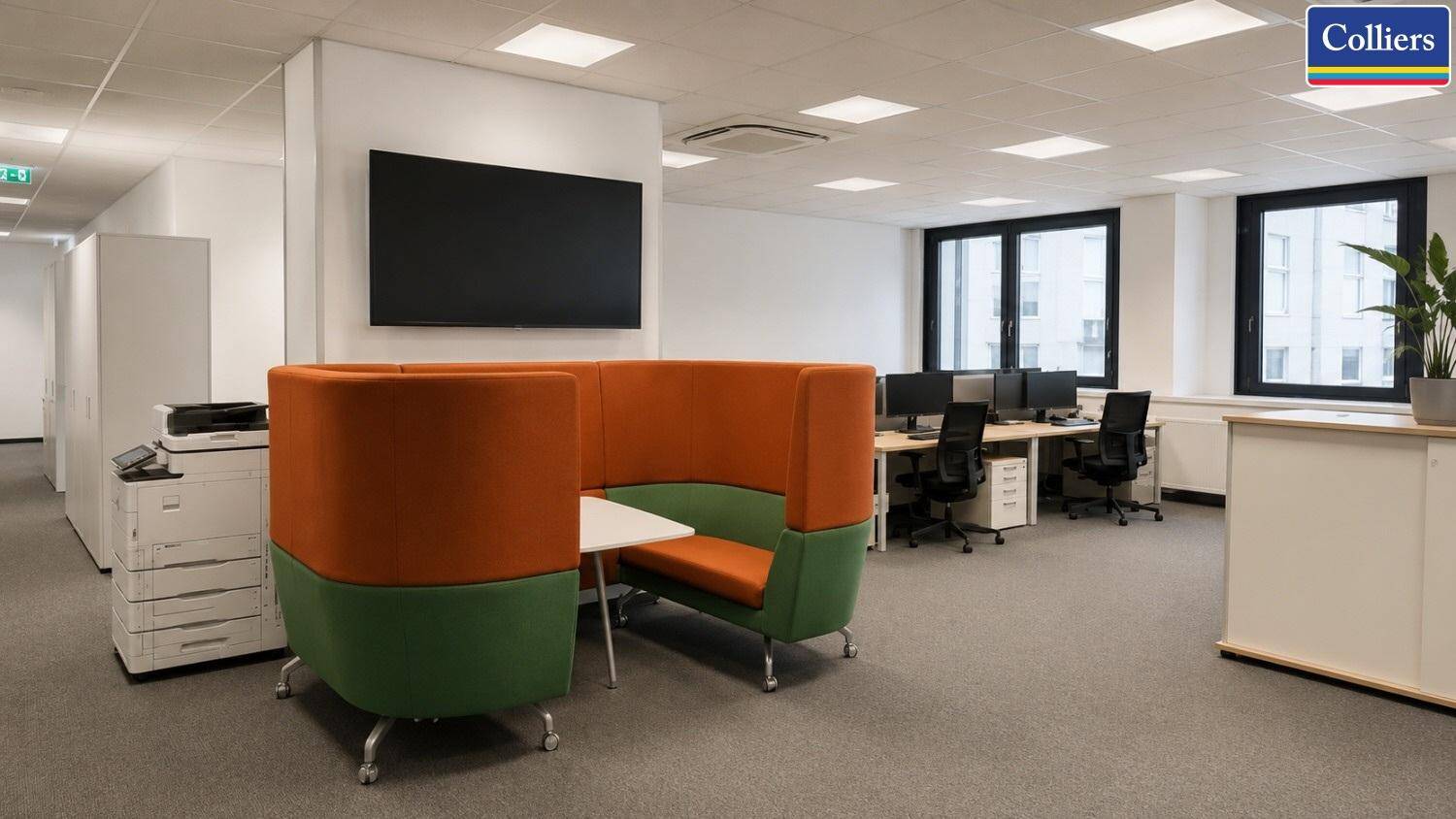 Offener Bürobereich mit farbigen Sitzgelegenheiten, Schreibtischen und einem Drucker, bietet flexible Arbeitsbereiche.