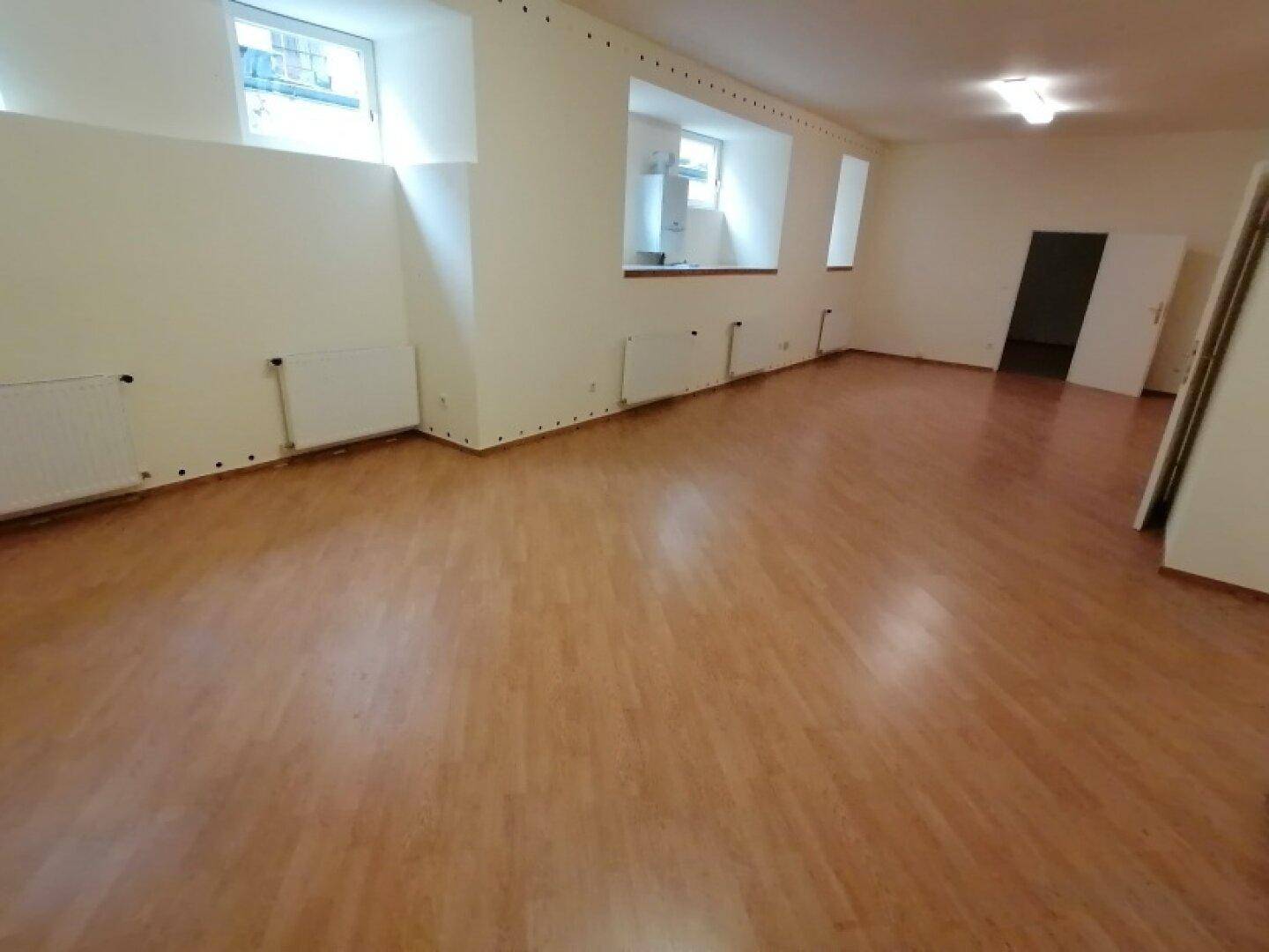 Geräumiger Raum mit Laminatboden, mehreren Fenstern und Heizkörpern, bietet viel Tageslicht und ist gut erhalten.