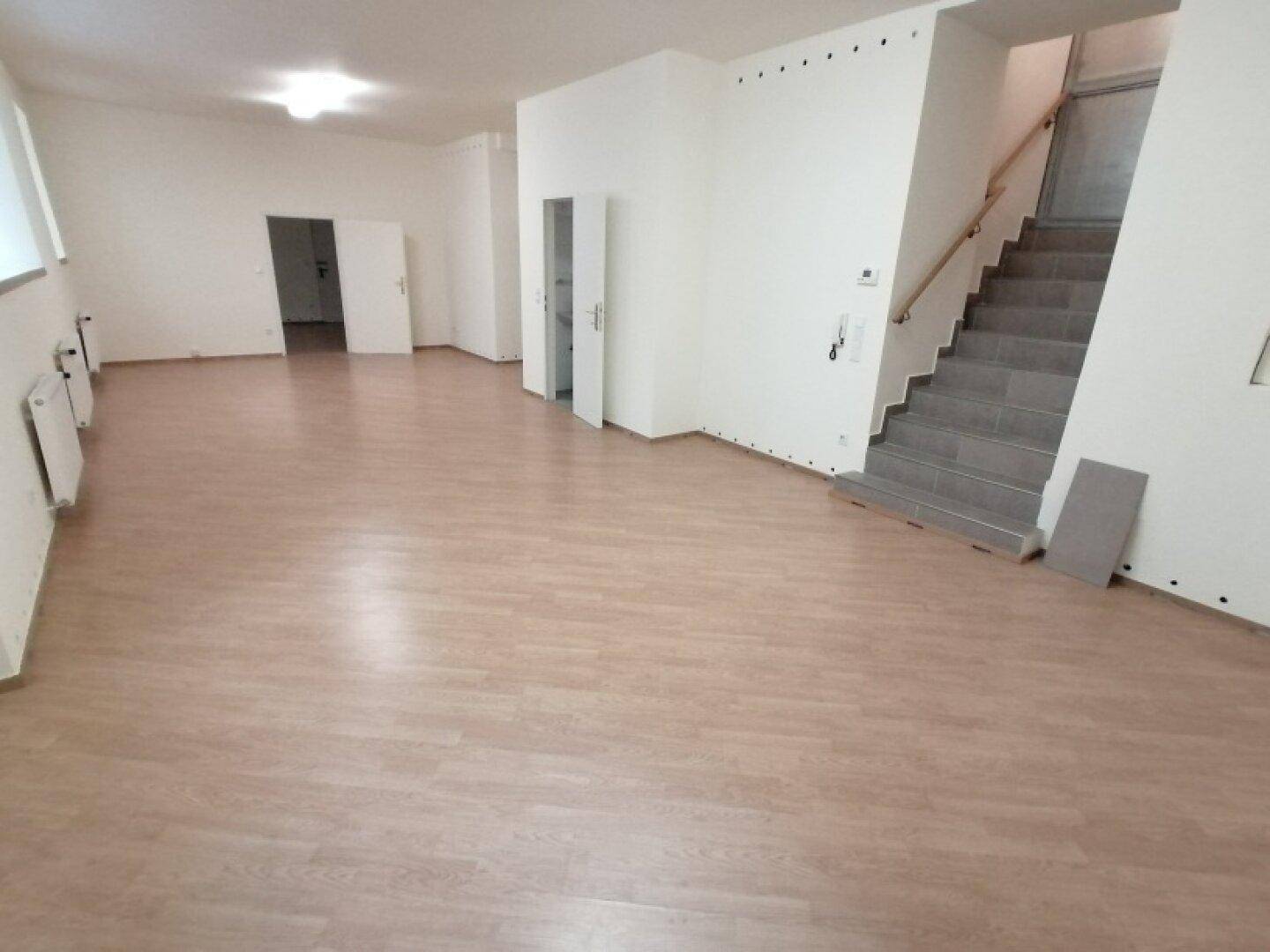 Heller, leerer Raum mit Laminatboden und Zugang zu einer Treppe, bereit zur individuellen Gestaltung und Nutzung.