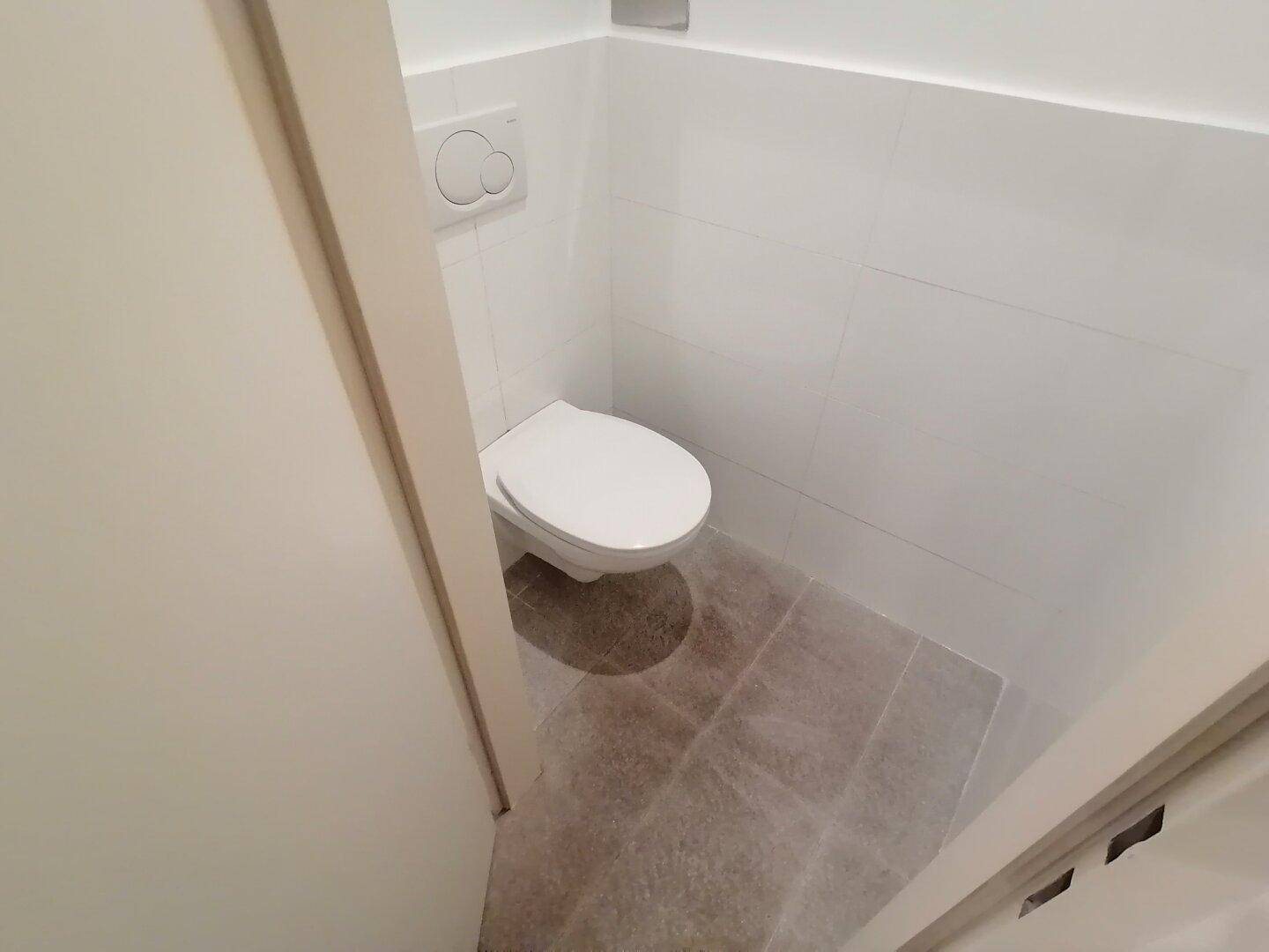 Sauberes Gäste-WC mit Wand-WC und weißen Fliesen an Wänden und Boden, in einem modernen und gepflegten Zustand.