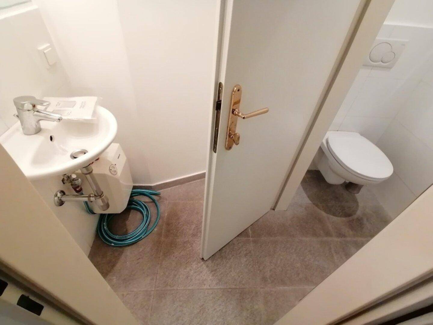Modernes Gäste-WC mit kleinem Waschbecken und Wand-WC, ausgestattet mit hellen Fliesen und minimalistischem Design.
