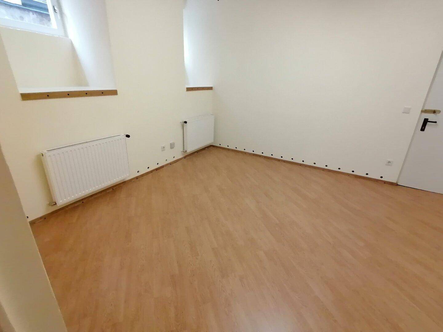 Kleinerer, heller Raum mit Laminatboden, einem Fenster und Heizkörper, ideal als Schlaf- oder Arbeitszimmer in gutem Zustand.