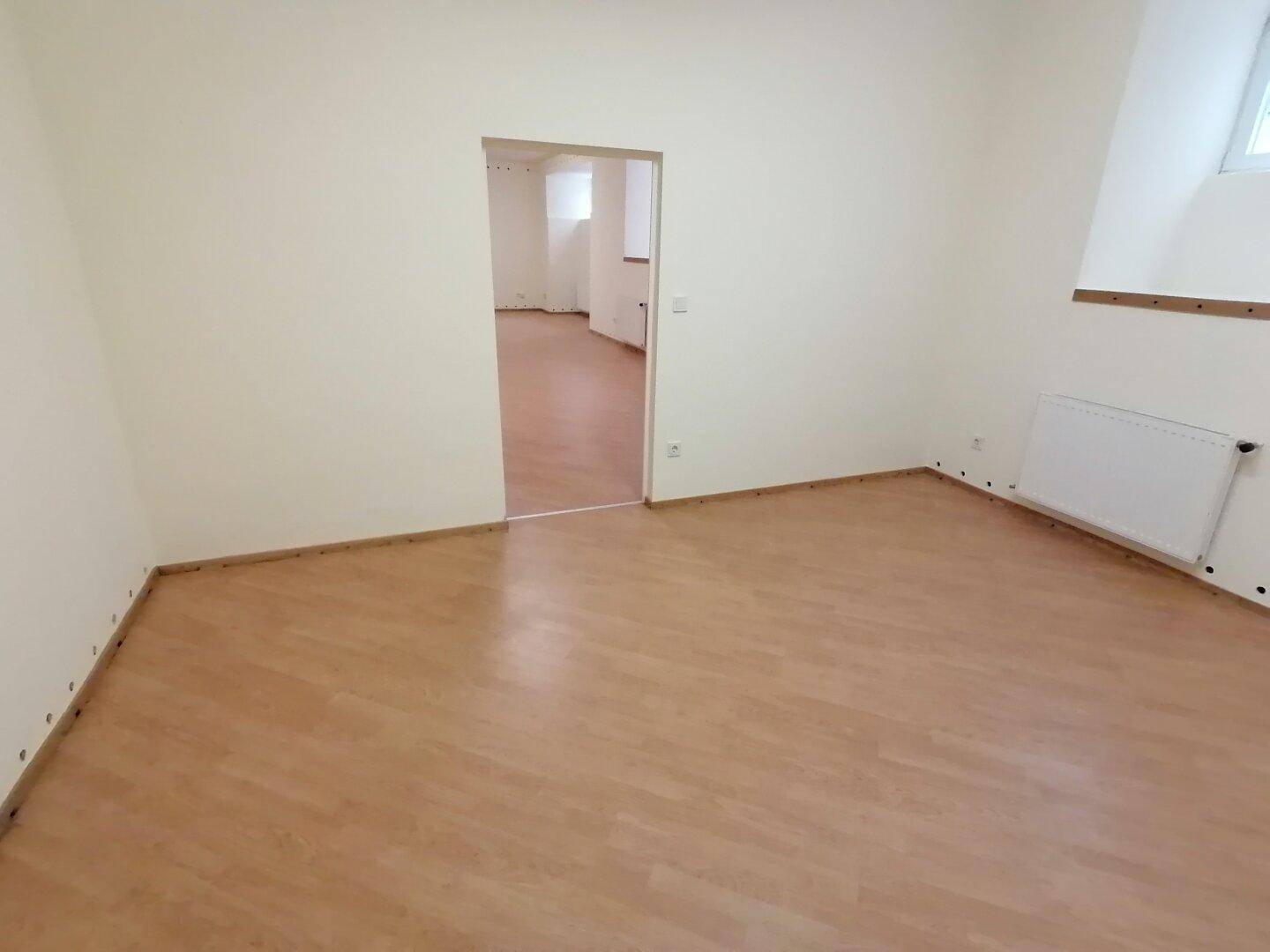 Heller Raum mit Laminatboden und offener Tür zu einem weiteren Zimmer, bietet flexible Nutzungsmöglichkeiten und ist gepflegt.