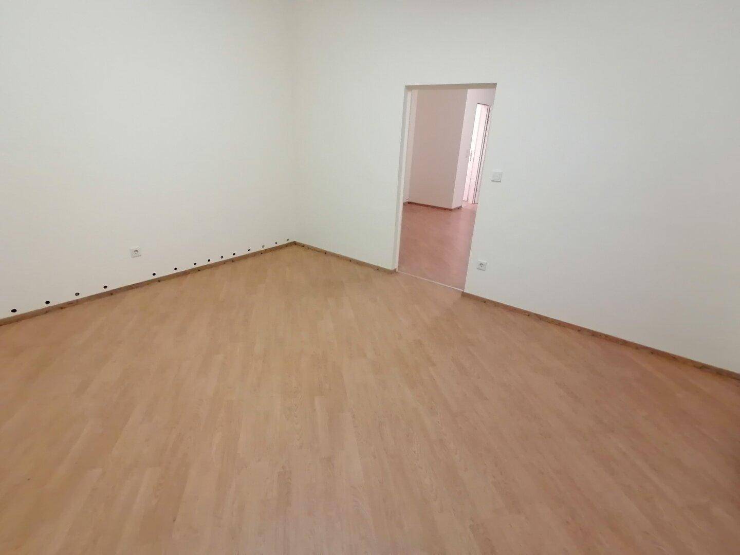 Leerer Raum mit Laminatboden und weiß gestrichenen Wänden, bereit zur individuellen Einrichtung und Nutzung.