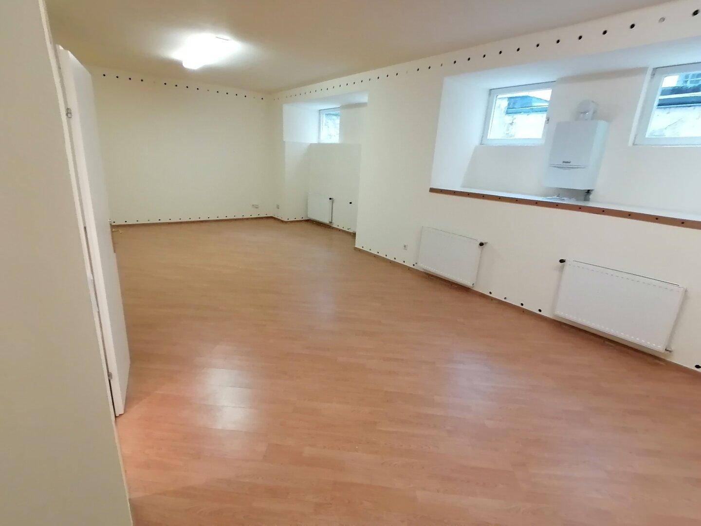 Geräumiger Raum mit Laminatboden, Fenstern und einem Heizkessel, vielseitig nutzbar und gut beleuchtet.