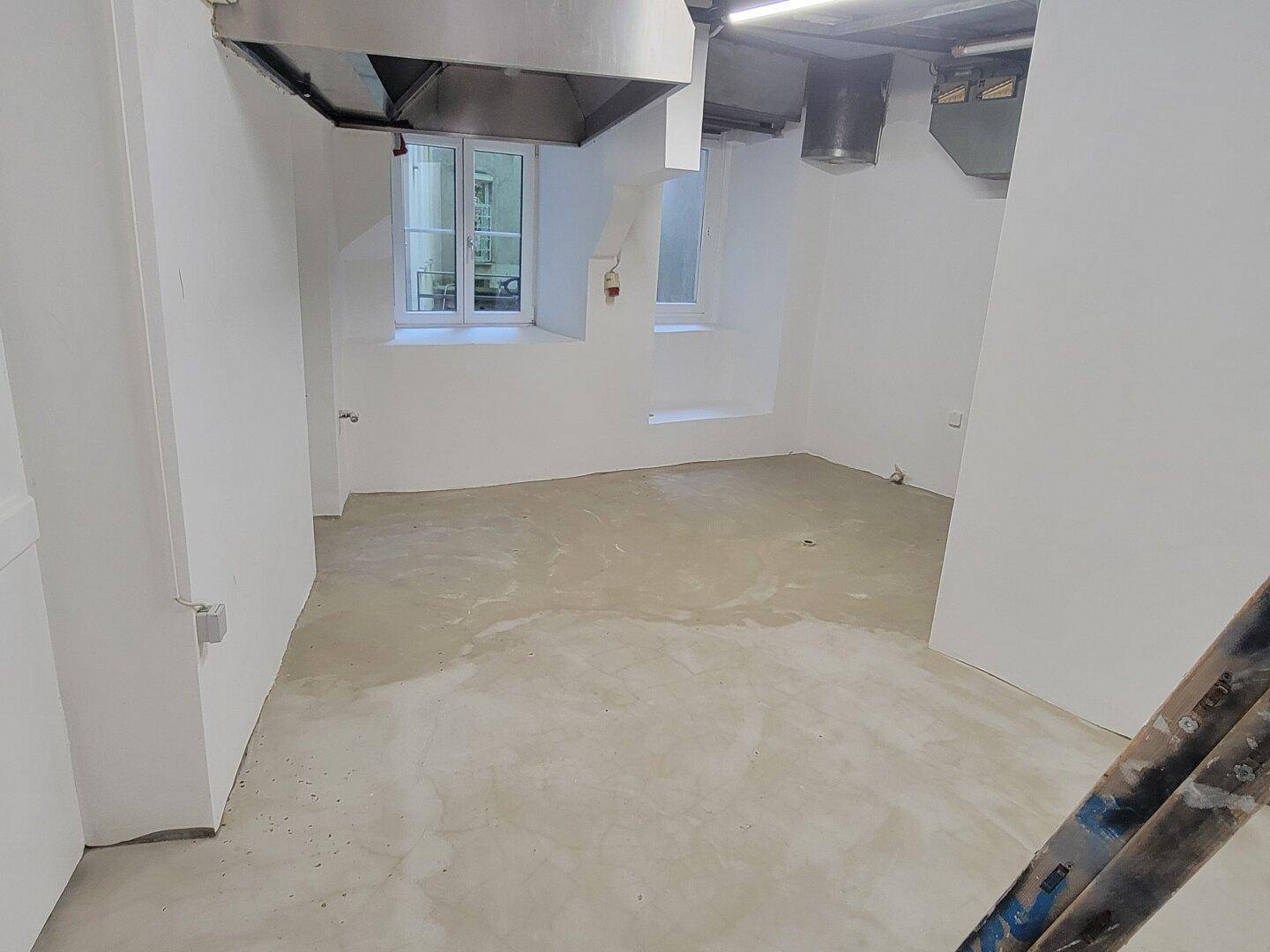 Leerer Raum mit Betonboden, weißen Wänden und großen Ablufthauben, ideal für eine Gewerbeküche.