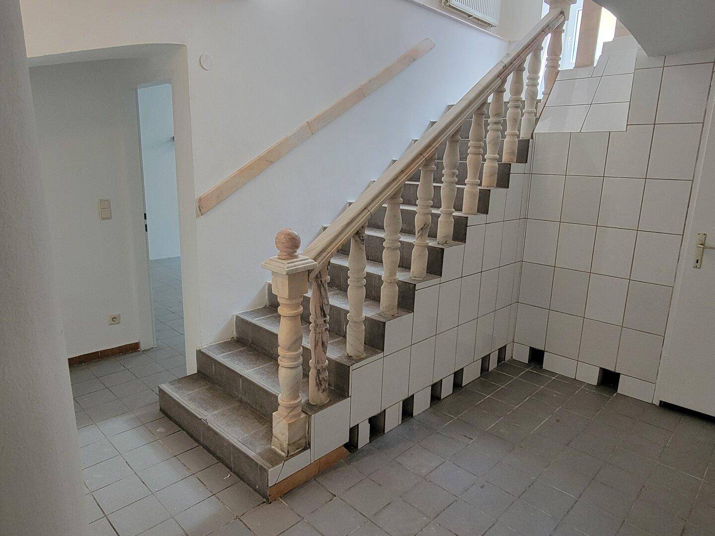 Treppenhaus mit gefliesten Wänden und Boden sowie einem Holzgeländer, das in die oberen Etagen führt.