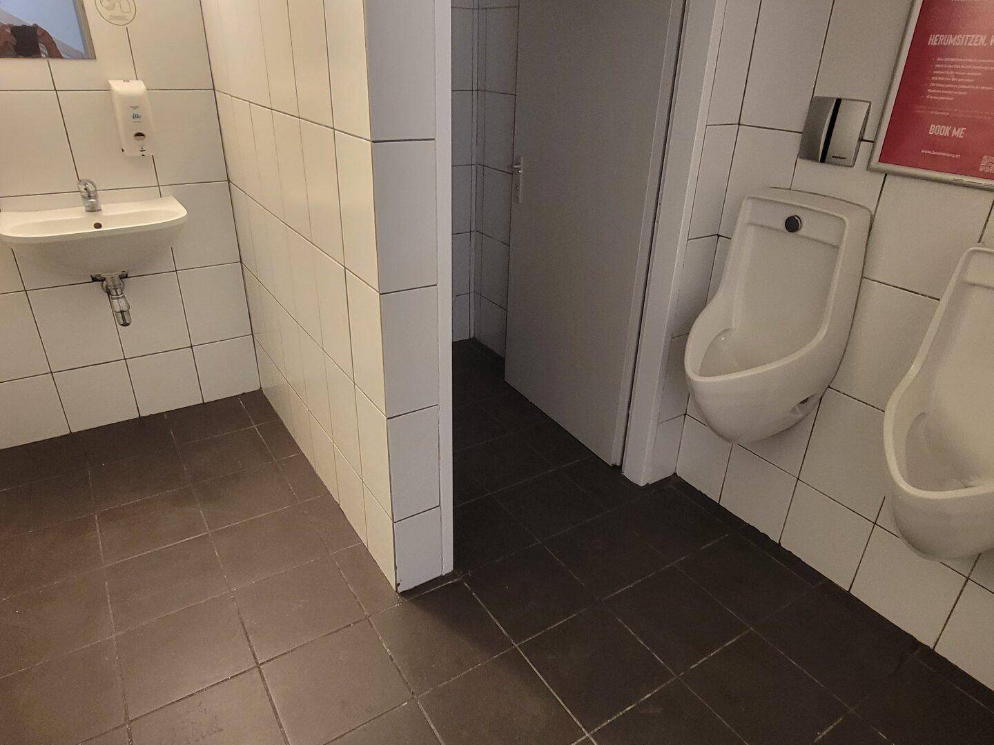 Herren-Waschraum mit Urinalen, Waschbecken und weißen Fliesen an den Wänden, in gutem Zustand.