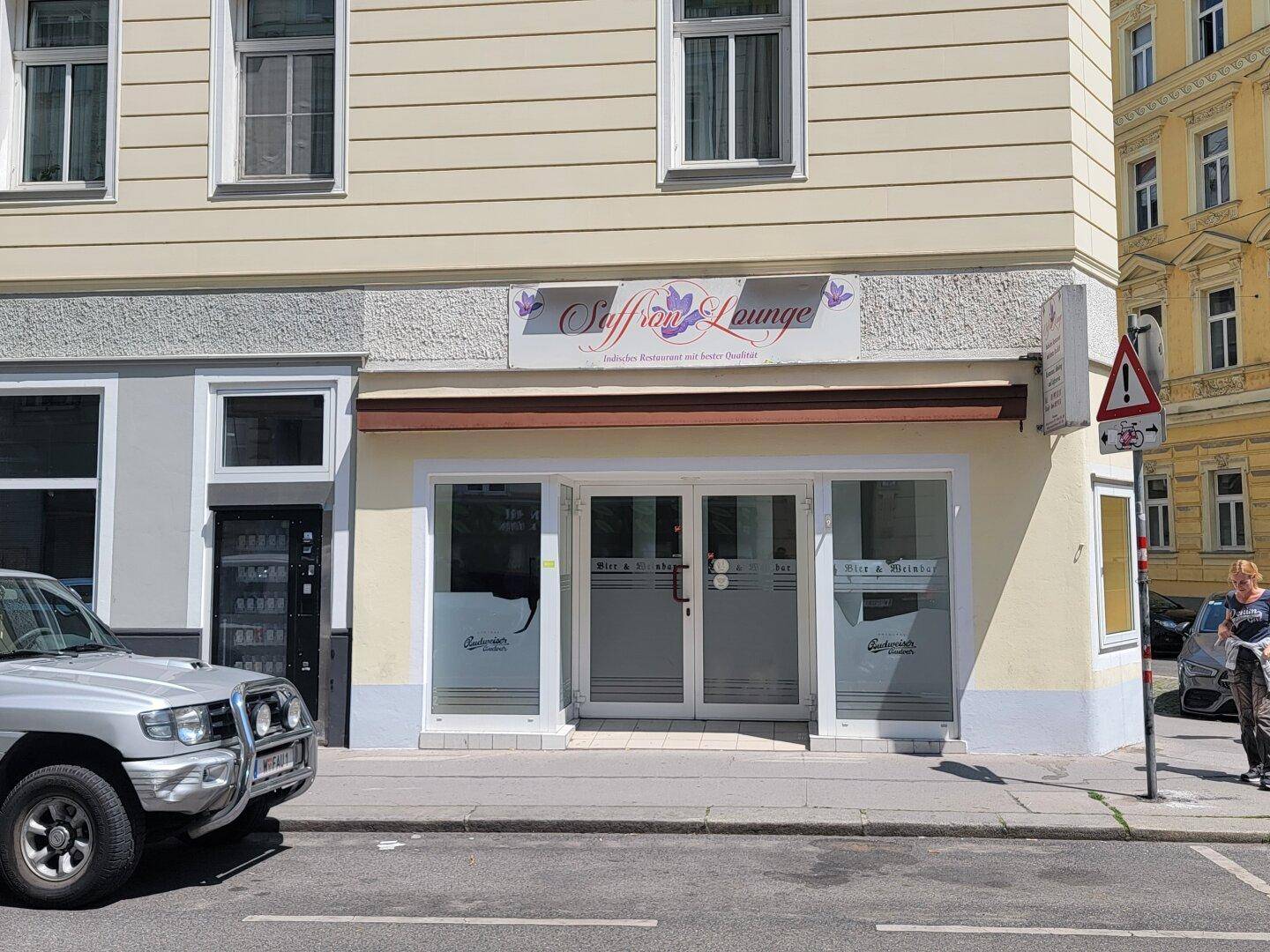 Fassade eines Geschäftsgebäudes mit großen Schaufenstern und einem geparkten Auto davor an einem sonnigen Tag.
